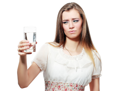 Femme regardant un verre d’eau avec scepticisme