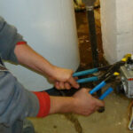 Fontanero usando dos llaves para apretar una conexión de tubería, ilustrando la falta de formación técnica.